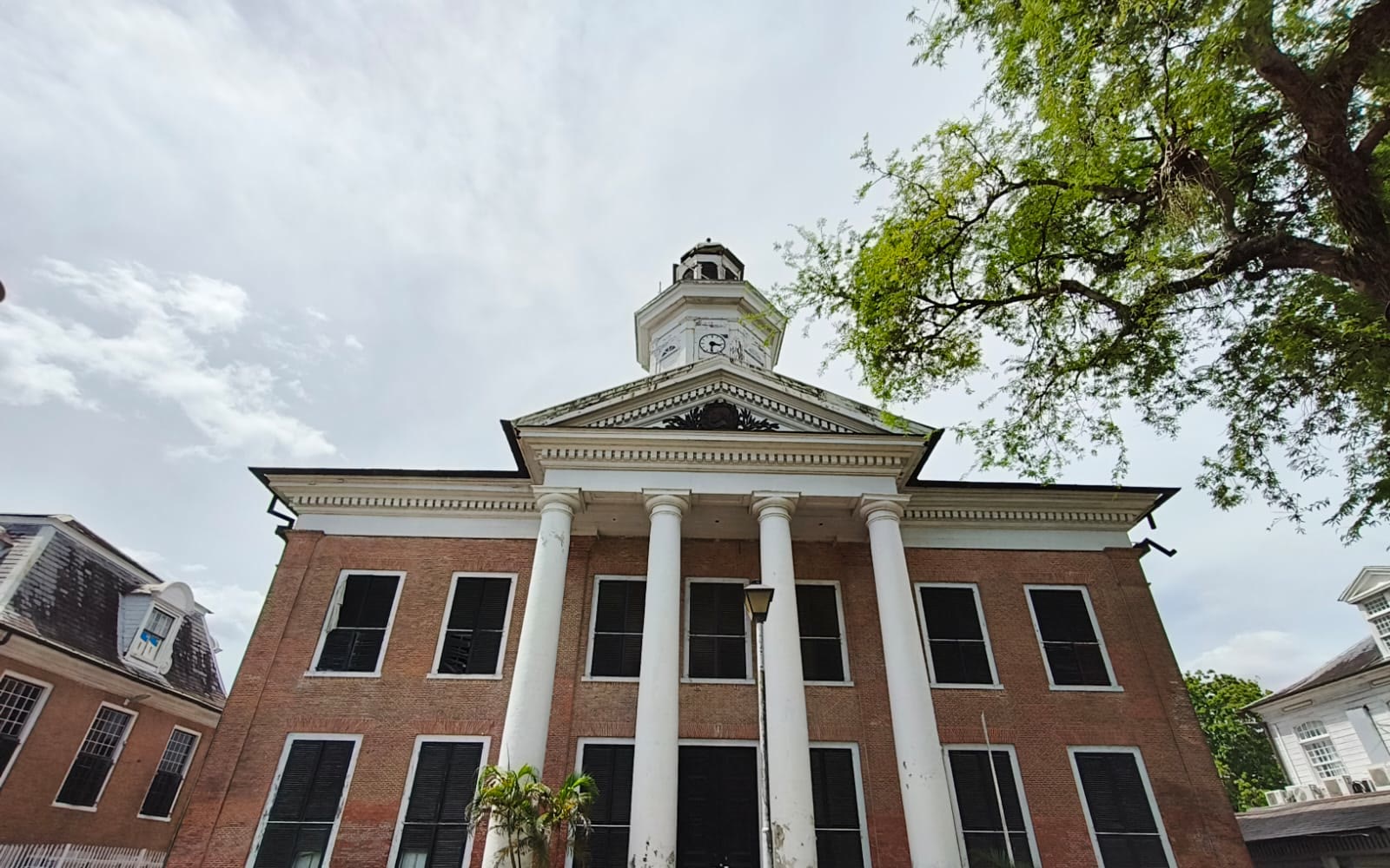 Brick building with white columns and a clock tower on Onafhankelijkheidsplein, Paramaribo, under a cloudy sky