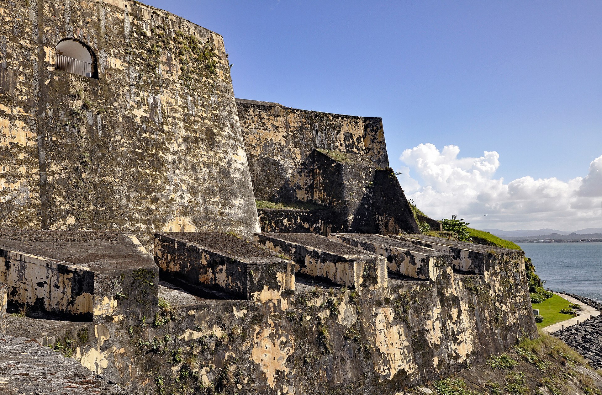 Weathered stone walls and gun platforms of El Morro fortress in San Juan beside the bay under a blue sky